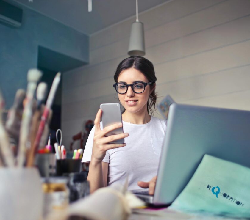 woman in white t shirt holding smartphone in front of laptop