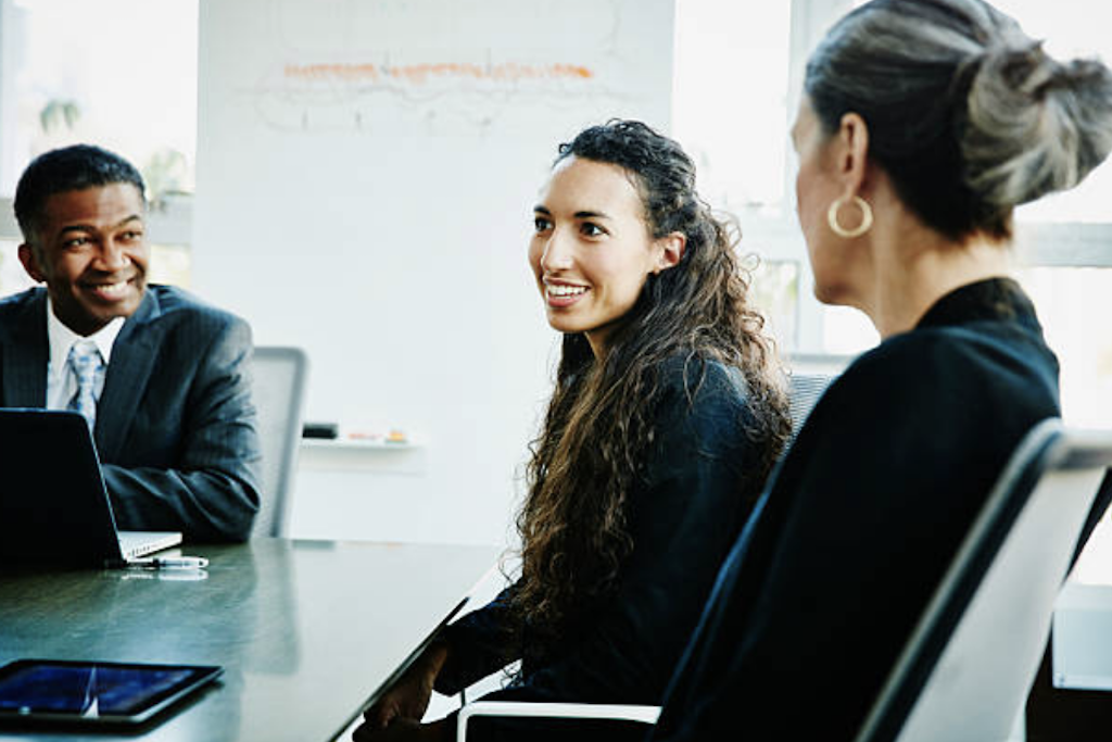 Professional PR manager leading virtual team meeting in modern office setting, displaying multiple digital communication channels.