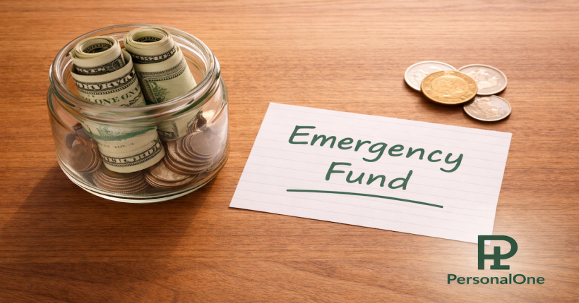 Glass jar partially filled with bills and coins beside a handwritten emergency fund note on a warm wood surface