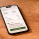 Smartphone displaying a financial dashboard with an AI insight card showing a spending pattern alert on a warm wood desk