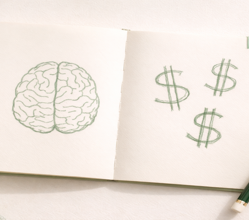 An open notebook with a simple hand-drawn brain sketch beside dollar signs, representing the connection between money psychology and financial behavior — how the brain drives spending decisions, emotional triggers, and the patterns that keep most budgets from working