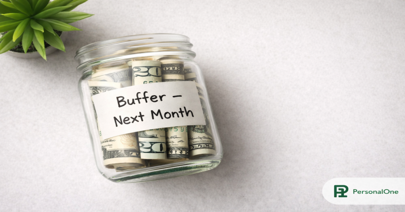 Glass jar two-thirds full of rolled bills labeled Buffer Next Month on a light gray surface — PersonalOne